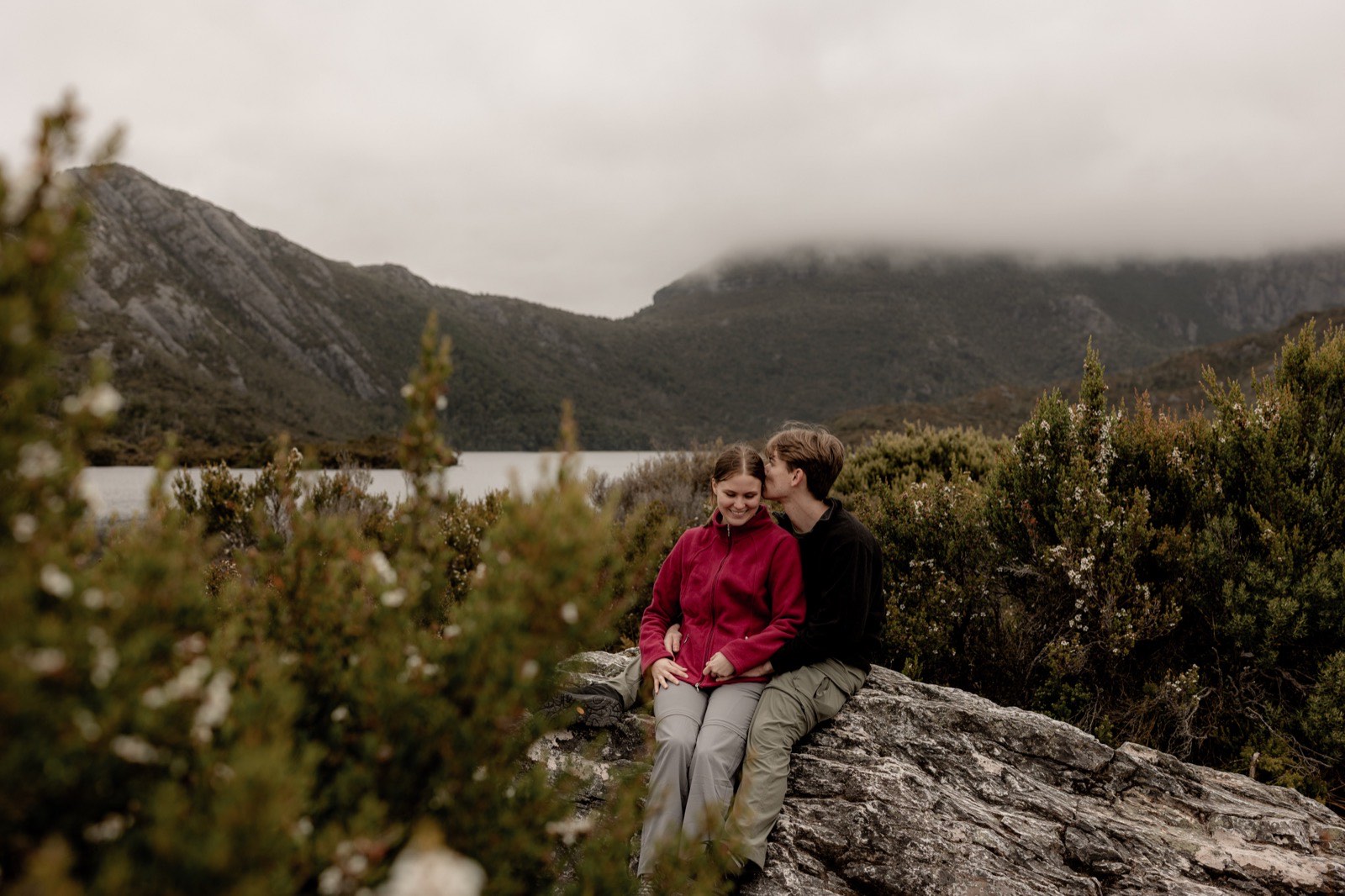 Engaged couple sitting on a rock among alpine scrub above Dove Lake, Cradle Mountain